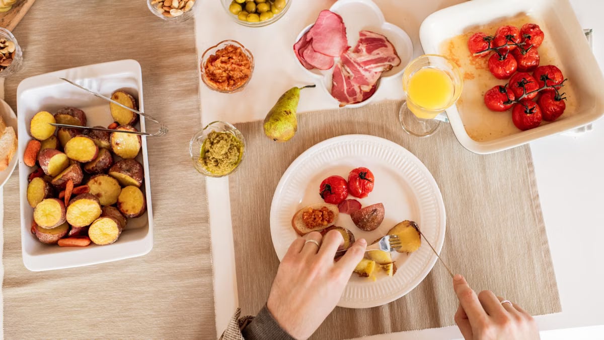 Top-down view of a vibrant brunch spread featuring roasted potatoes, tomatoes, cold cuts, and fresh juice.